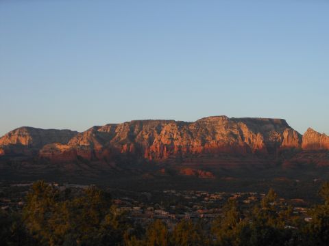 1995 Ford Bronco - The sun casts a warm glow on the layered rock formations of a mountain range, with trees and buildings visible below.