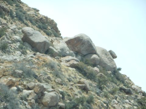 1995 Ford Bronco - A rocky hillside with scattered bushes under a clear sky, a watermark at the bottom right.