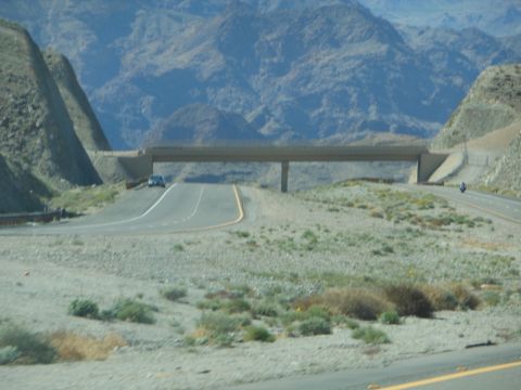 1995 Ford Bronco - A car travels on a highway passing under a bridge in a vast, arid, mountainous region.