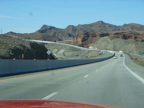 1995 Ford Bronco - A scenic highway winds through mountainous terrain under a clear blue sky, with several vehicles visible on the road.
