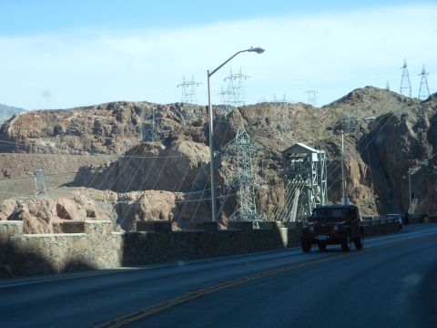 1995 Ford Bronco - A red SUV travels along a road with a large dam and power infrastructure visible in the rocky landscape.