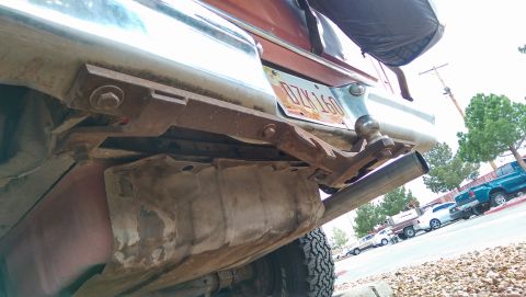 1978 Ford Bronco - View of a trailer hitch assembly and exhaust pipe on a vehicle, with other cars in the background.