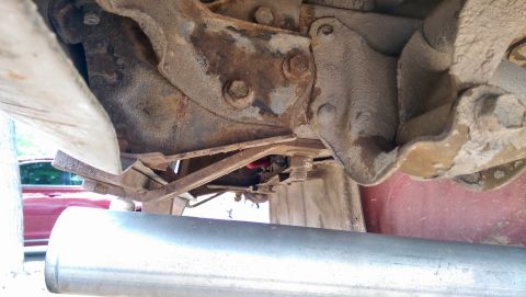1978 Ford Bronco - The underside of a red vehicle shows a large exhaust pipe and heavily rusted suspension parts.