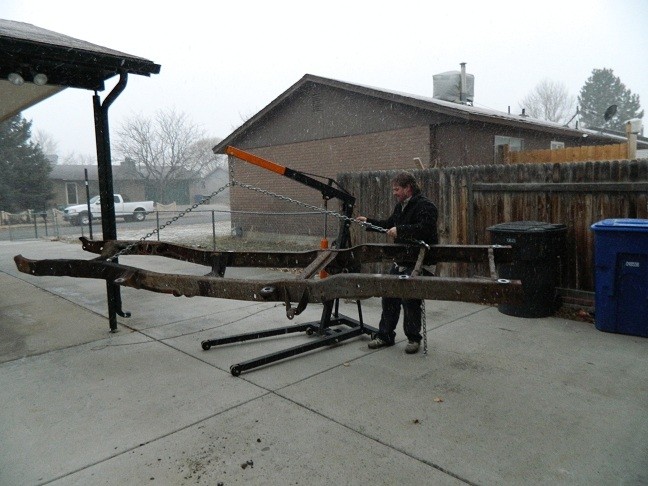 Rusty vehicle frame on an engine hoist during snowfall