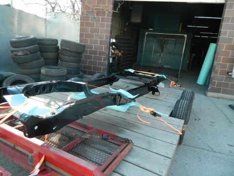 1979 Ford Bronco - A vehicle frame is prepared for transport on a trailer, with numerous tires stacked nearby.