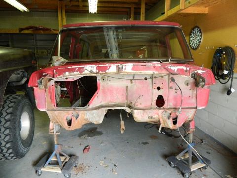 1979 Ford Bronco - The front end of a red Ford Bronco is disassembled and supported by jack stands in a garage.