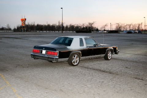 1985 Mercury Grand Marquis - Rear three-quarter view of a black and silver 1985 Mercury Grand Marquis in an open lot.