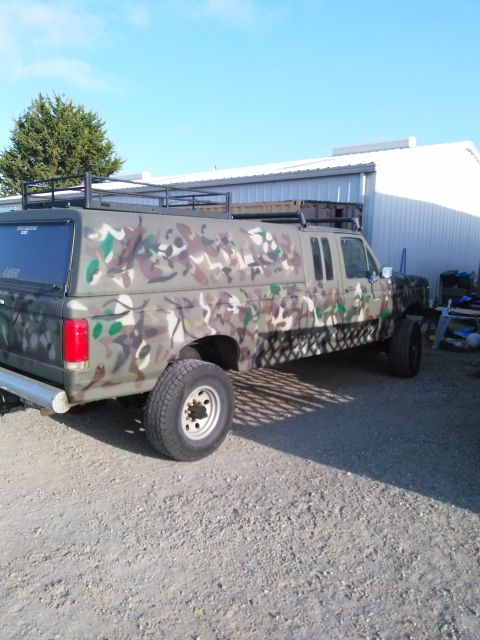 1991 Ford Bronco - This extended cab pickup truck features a camouflage paint job and a camper shell with a roof rack.