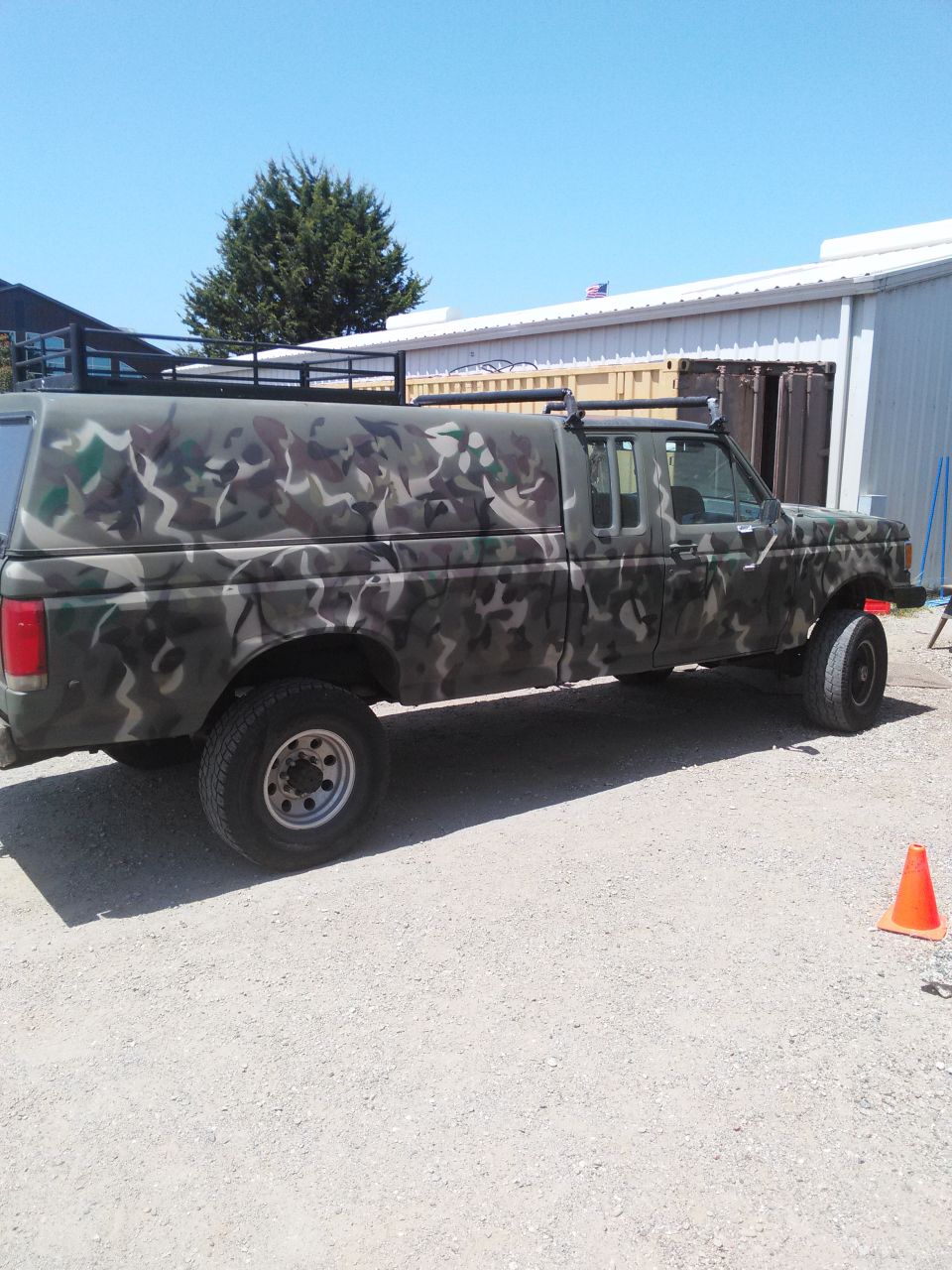 Side view of a 1991 Ford F-150 pickup truck painted in camouflage, with a camper shell and roof rack