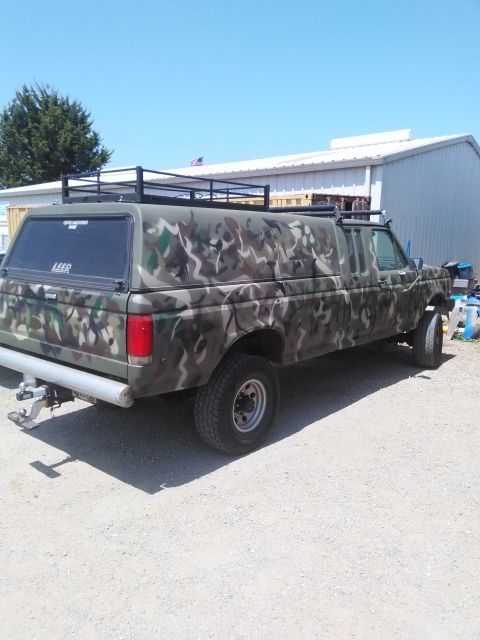 1991 Ford Bronco - This truck has a camouflage paint job and a camper shell with a roof rack.