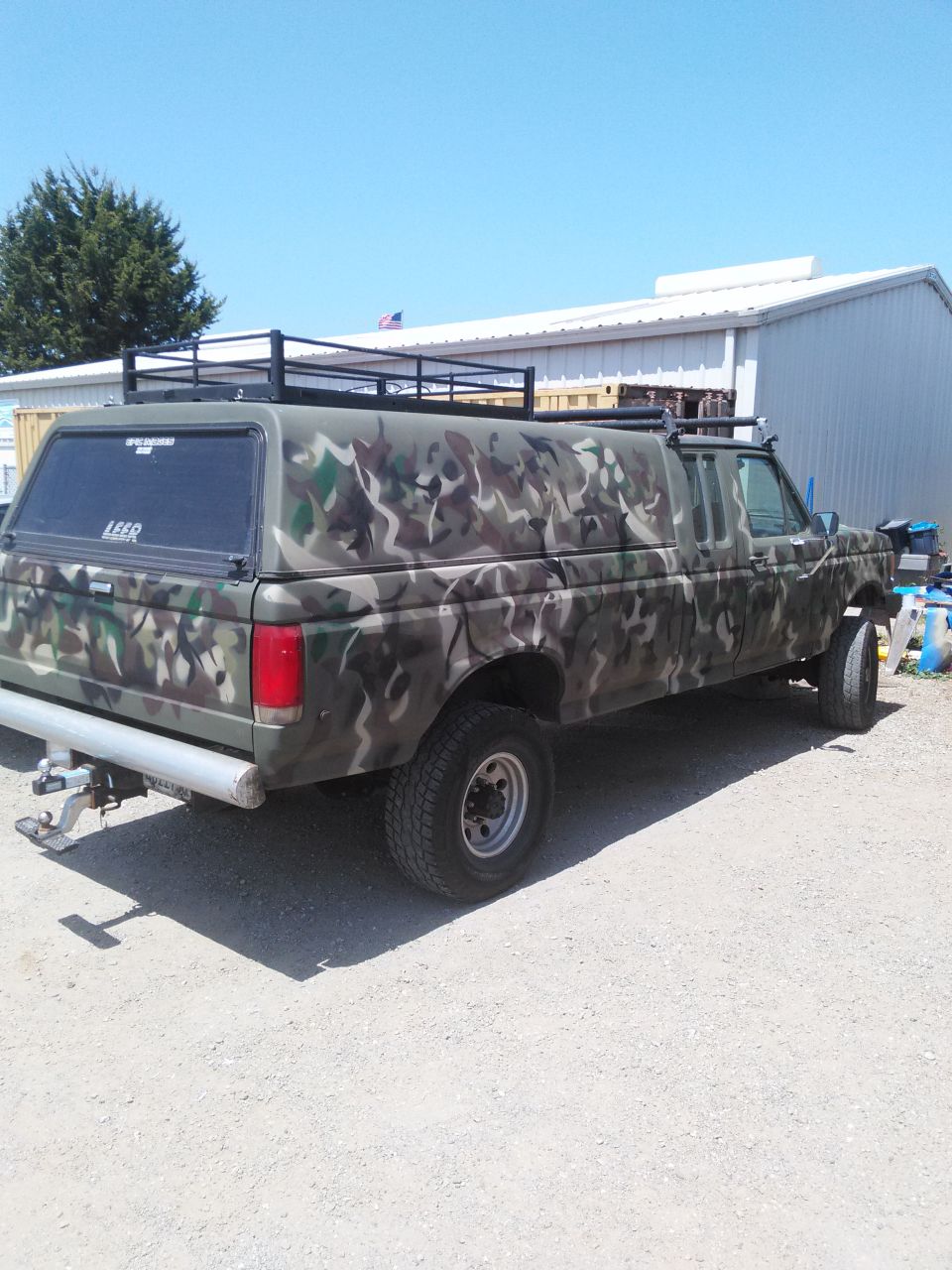 Pickup truck with camouflage paint, camper shell, and roof rack
