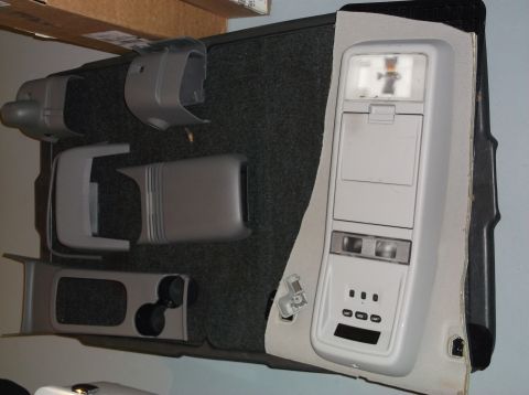 1999 Mercury Grand Marquis - Disassembled car interior console parts and overhead light assembly are laid out on a dark carpeted surface.