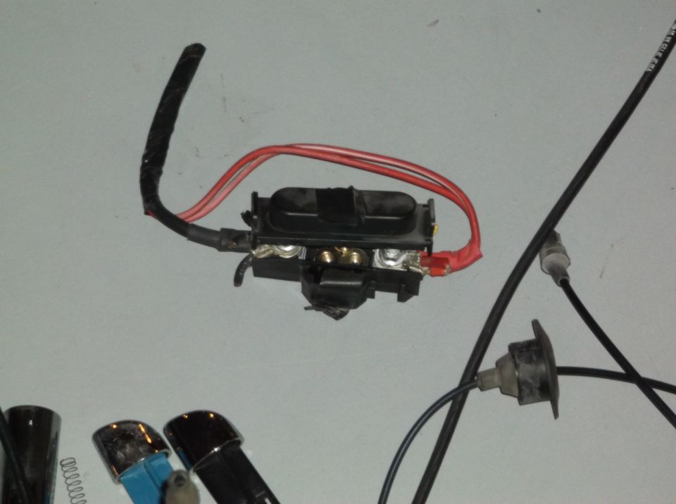 Automotive fuse box with red and black wires attached to terminals, against a light gray background