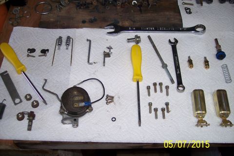 1973 Ford F-250 - Various carburetor parts, including floats, jets, screws, and tools, are organized for a rebuild.