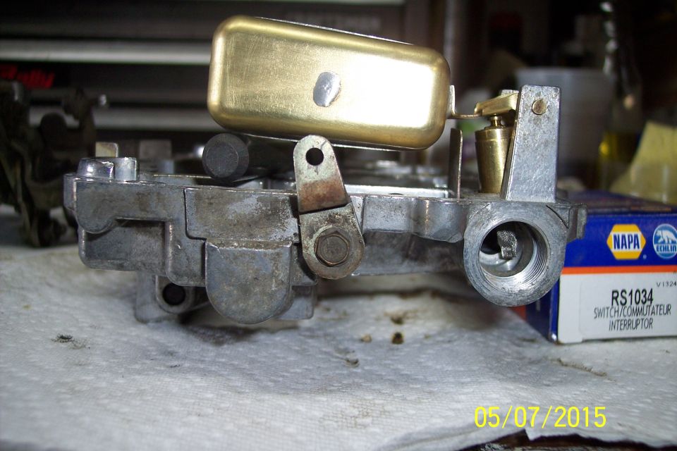 Close-up of a carburetor with a brass float and linkage. NAPA RS1034 box visible