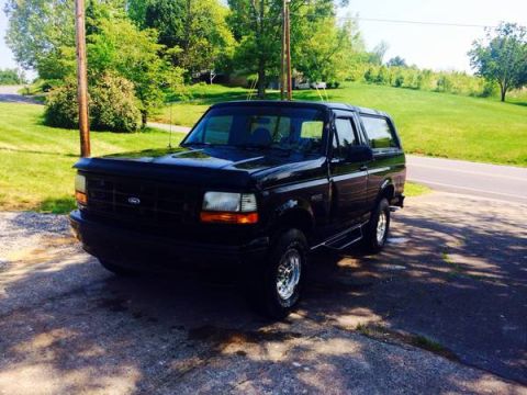 1996 Ford Bronco - A black 1996 Ford Bronco is parked on a paved surface with a grassy area and trees behind it.