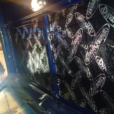 1978 Ford Bronco - Dynamat sound deadening material is applied to the interior wall of a blue vehicle, covering the surface with its distinctive logo.