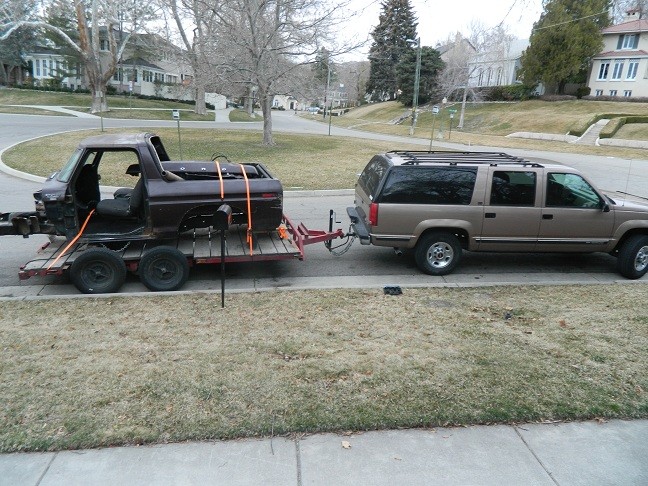 Brown 1979 Ford Bronco on trailer, side view. Towed by tan SUV