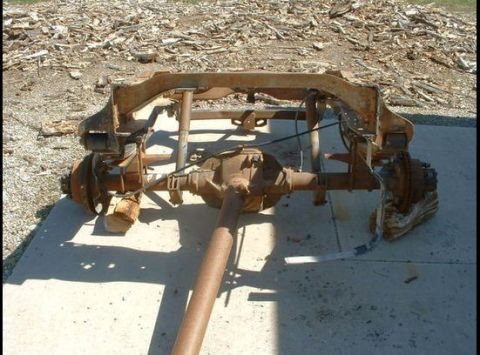 1979 Ford Bronco - This is a rear view of a heavily rusted vehicle chassis and axle assembly, resting on a concrete surface.