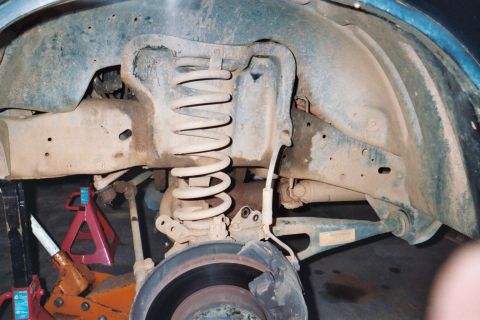 1988 Ford Bronco - Close-up of a vehicle's front suspension and brake components, supported by jack stands.