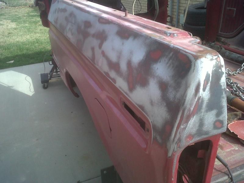 Red vehicle quarter panel with primer and body filler, showing repair work