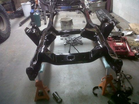 1979 Ford Bronco - A vehicle frame is supported by jack stands in a workshop environment.