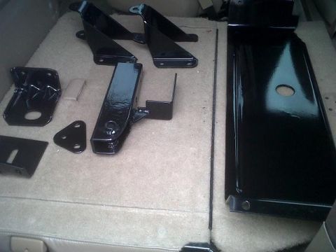 1979 Ford Bronco - Various black metal parts, possibly for a vehicle, are laid out on a tan carpeted surface.