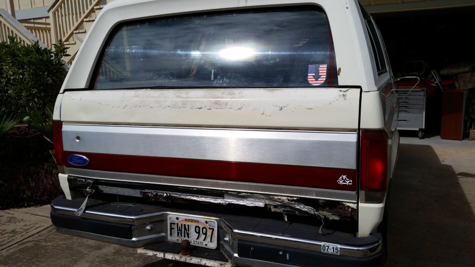 Rear view of a white 1990 Ford Bronco with a damaged bumper and a US flag sticker
