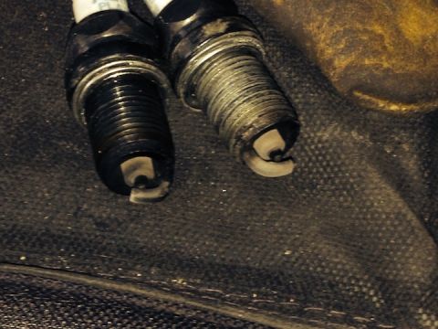 1961 International Scout 800 - Close-up of two used spark plugs, one with heavy carbon buildup and the other showing significant wear on the electrode.