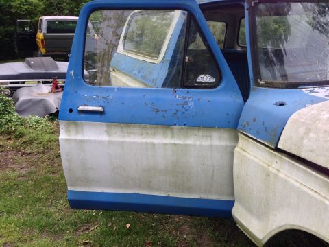 1979 Ford Bronco - Side view of a weathered 1979 Ford Bronco door, with another vehicle in the background.