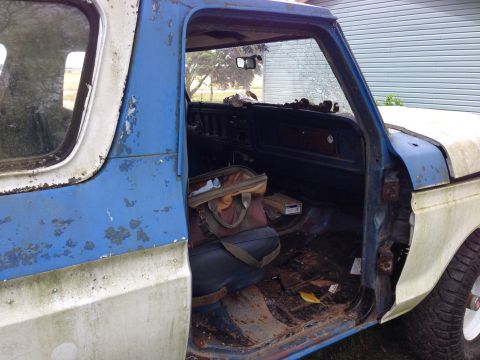 1979 Ford Bronco - The interior of a weathered pickup truck shows a worn seat and floor with a bag placed on the driver's side.