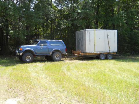 1992 Ford Bronco - Blue Ford Bronco tows a large cargo trailer through a grassy area.