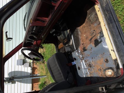 1988 Ford Bronco II - The interior of a vehicle shows significant rust on the floor and missing passenger seat, with the dashboard and steering wheel in view.
