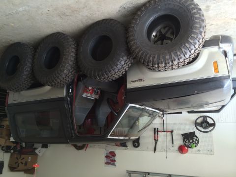 1988 Ford Bronco II - A 1988 Ford Bronco II is shown with its doors open and four large off-road tires stacked on its roof.