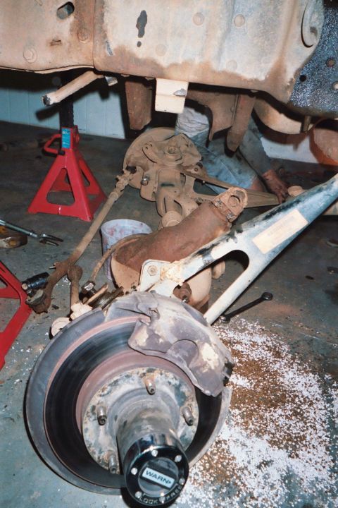 1988 Ford Bronco - Front suspension and brake assembly with a Warn locking hub. Vehicle is on jack stands.