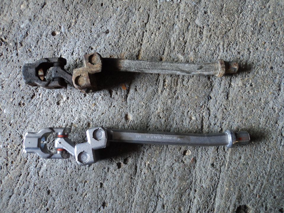 Old rusty steering shaft u-joint next to a new shiny one