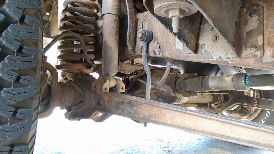 Close-up of vehicle's front suspension, shock absorber, coil spring, and driveshaft