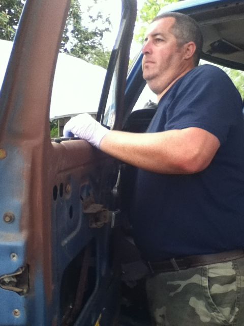 1979 Ford Bronco - A man works on the interior of a weathered blue vehicle, showing signs of rust on the door panel.