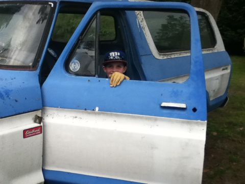1979 Ford Bronco - A young boy sits in the driver's seat of a blue and white 1979 Ford Bronco, with the driver's door open.