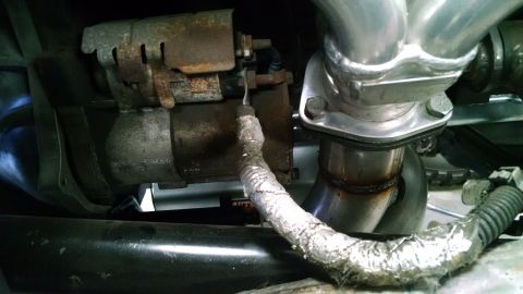 1985 Jeep CJ7 - Close-up view of a starter motor and exhaust manifold, with a portion of the exhaust pipe wrapped in heat insulation material.