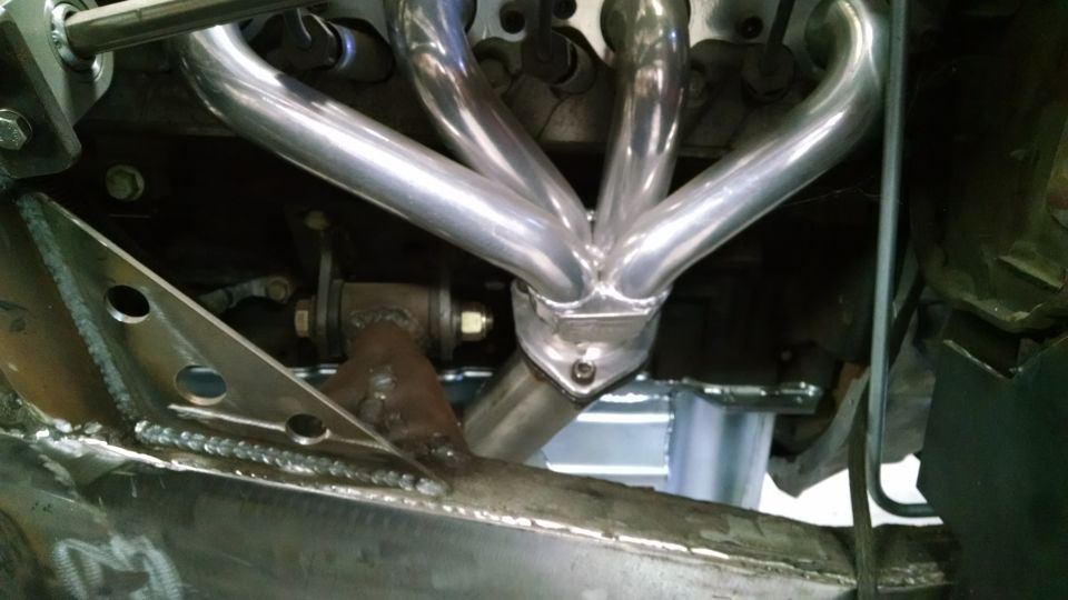 Close-up of shiny exhaust headers on an engine, with custom metal fabrication visible below