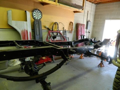 1979 Ford Bronco - The chassis of a vehicle is elevated on jack stands in a garage, surrounded by various automotive parts.