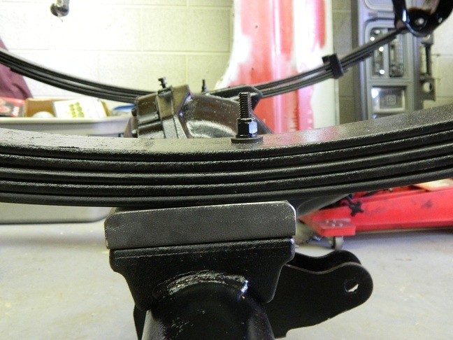 Leaf spring assembly held in a vise, with a bolt securing the spring stack
