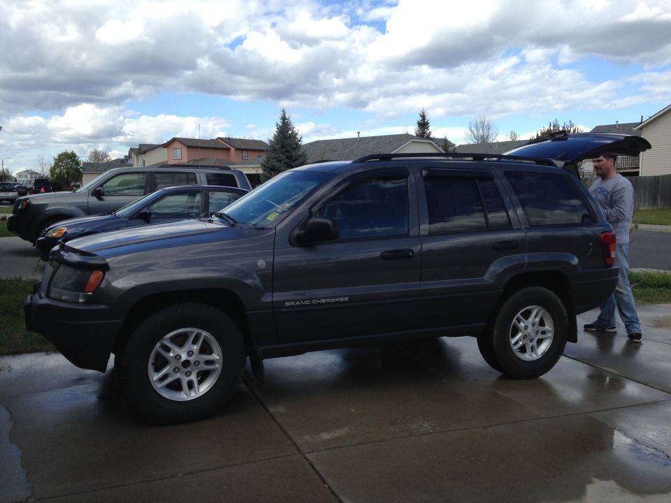 Dark gray 2004 Jeep Grand Cherokee parked in a driveway, rear hatch open. Another SUV and a sedan are parked behind it