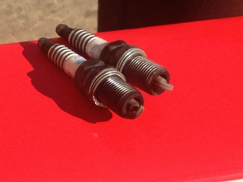 1961 International Scout 800 - Two spark plugs are shown on a red surface, casting shadows.