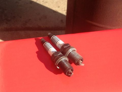 1961 International Scout 800 - Two spark plugs are shown resting on a red surface under bright sunlight.