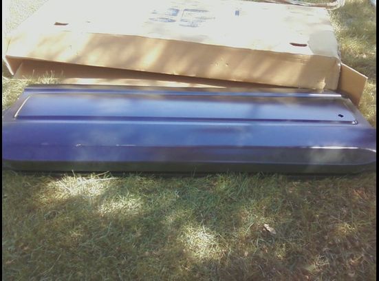 Dark blue car door panel lying on grass with a cardboard box behind it