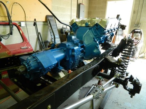 1979 Ford Bronco - Engine and transmission assembly undergoing work on a vehicle chassis, with a red door visible in the background.