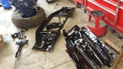 1978 Ford Bronco - Vehicle parts, including a frame and engine, are disassembled and laid out on the floor of a workshop.