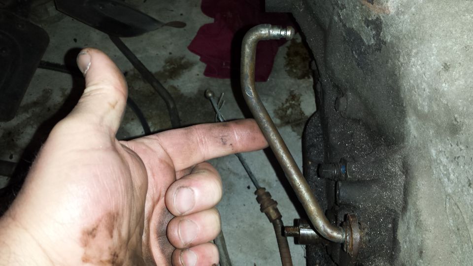 Hand pointing to a metal tube connected to a greasy engine block